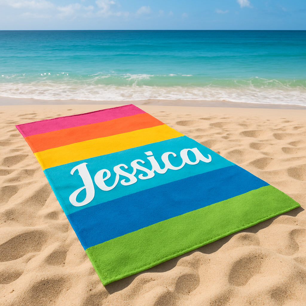 A vibrant custom beach towel with a monogramed name, laid out on sand with a seaside backdrop. Alt: custom beach towel with name gift
